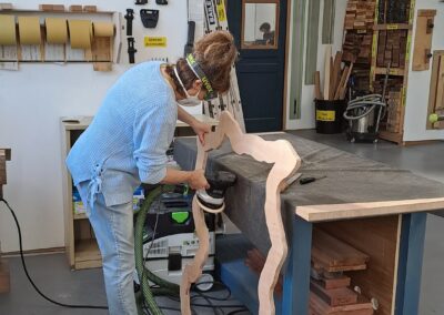 Student wearing mask and ear muffs sanding her unusual woodworking project