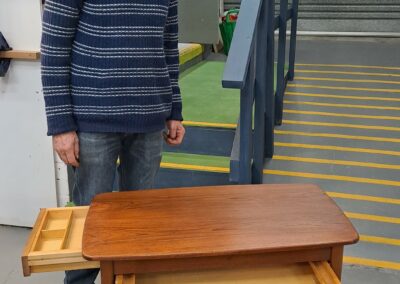 A happy furniture restoration student standing with his finished project